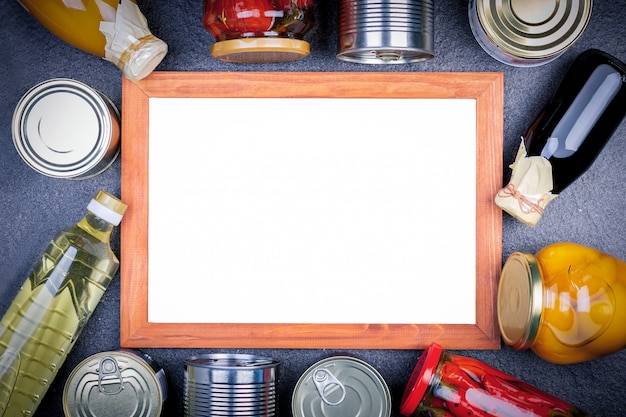 Various canned vegetables, meat, fish and fruits in tin and glass with board.