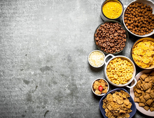 Various cereals in bowls on stone table.