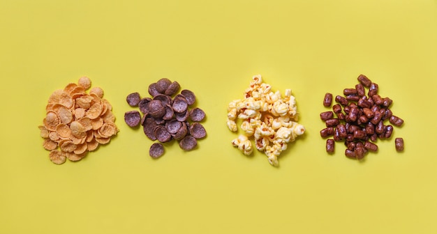Various cereals cornflakes snack and popcorn pile on yellow  top view for breakfast
