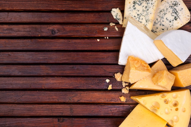 Various cheeses on wooden table with empty space.