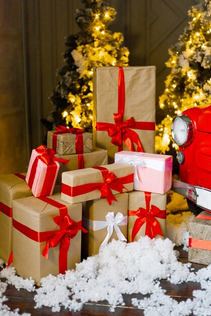 Различные рождественские подарки в крафтовой бумаге с лентами под освещенной елкой.