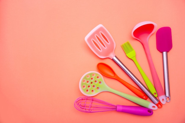 Various colored silicone kitchen utensils on coral background. copy space for your text