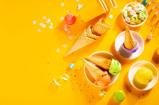 Various colorful ice cream scoops or balls with waffle cones on yellow background Top view Copy space