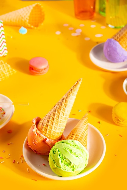 Various colorful ice cream scoops or balls with waffle cones on yellow background