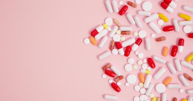 Various colorful medication tablets and capsules on pink background Concept of healthcare medicine