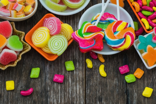 Various colorful sugary candy in container on old wooden plank