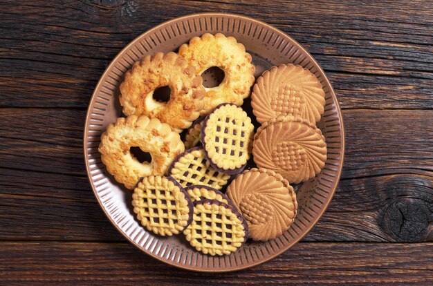 Various cookies in plate on old wooden table, top view