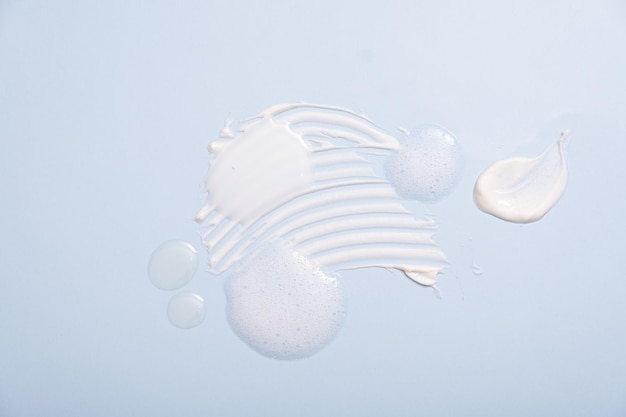 Various cosmetic smears on a blue background top view lather\
soap foam aloe vera clear transparent spot facial moisturizer body\
milk lotion and lipstick texture