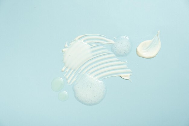 various cosmetic smears on a blue background top view lather soap foam aloe vera clear transparent spot facial moisturizer body milk lotion and lipstick texture