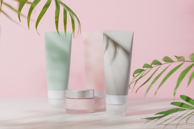 Various cosmetic tubes for serum cream and lotion on pastel pink background