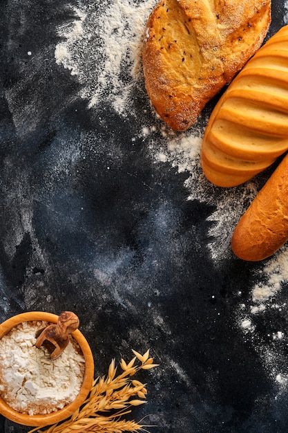 Various crispy breads and buns, wheat flour and ears on gray old concrete background table.