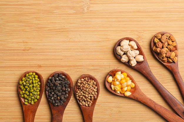 Various dried types of bean and pea in wooden spoon.