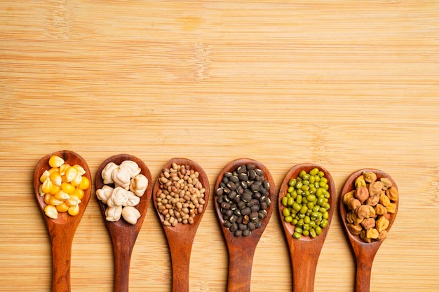 Various dried types of bean and pea in wooden spoon.