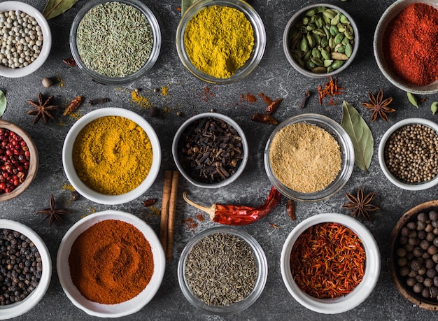 Various dry spices flat lay in small bowls on gray background. Top view, 