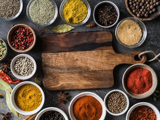 Various dry spices flat lay in small bowls and wood board on gray background. Top view, 