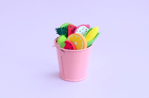 Various fresh fruits in small pink pail on violet background