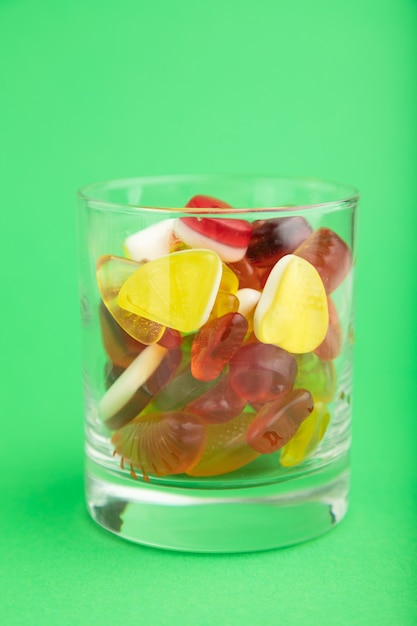 Various fruit jelly candies in drinking glass on green pastel background