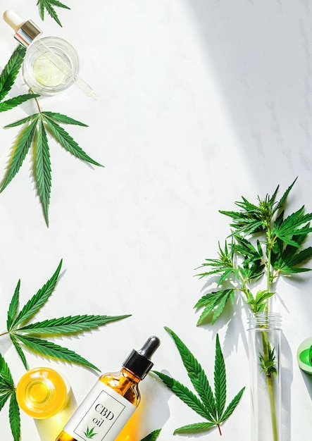 Various glass bottles with CBD oil, THC tincture and marijuana leaves on a marble