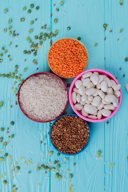 Various grain piles in plates. Scattered green split peas. Blue wood on background.