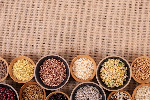 Various grains and cereals in small bowls on hemp background