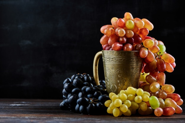 Photo various grapes in a metal glass on a dark wooden background