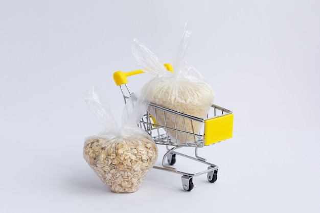 Vari semole in confezioni in un carrello della spesa su uno sfondo bianco. riso e farina d'avena