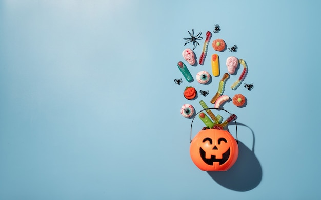 Various halloween sweets and candies in a pumpkin pot on blue solid background 