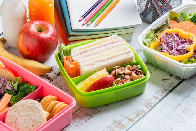 Photo various of healthy lunch boxes of sandwich. kid bento pack for school set in plastic package, salad box, banana and apple with orange juice, milk.