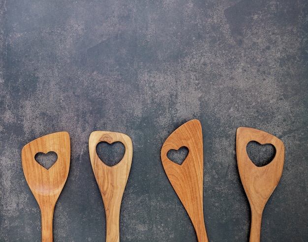Various heart shape of wooden cooking utensils on dark concrete background with flat lay and copy space