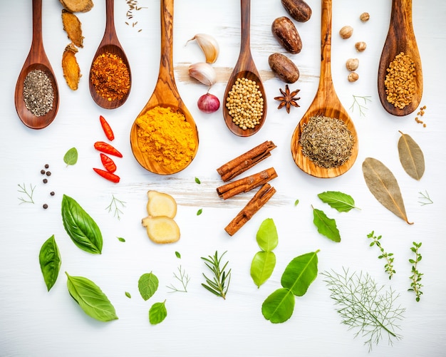 Various herbs and spices in wooden spoons on wooden background.