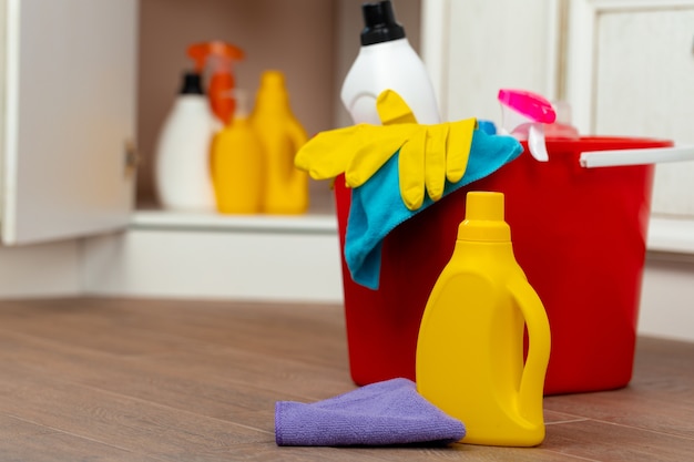 Various household cleaning detergents and bottles in a plastic bucket on the floor