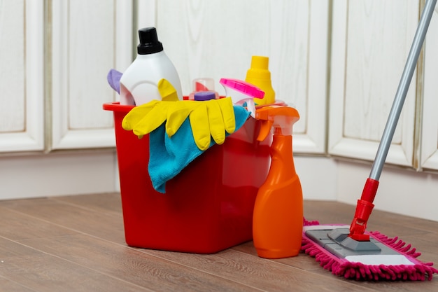 Various household cleaning detergents and bottles in a plastic bucket on the floor