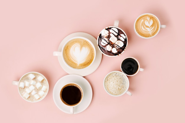 various kinds of coffee in cups of different size on pale pink background