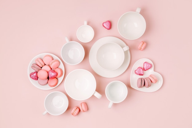 Various kinds of coffee in cups of different size with candys and macaroons on pale pink background