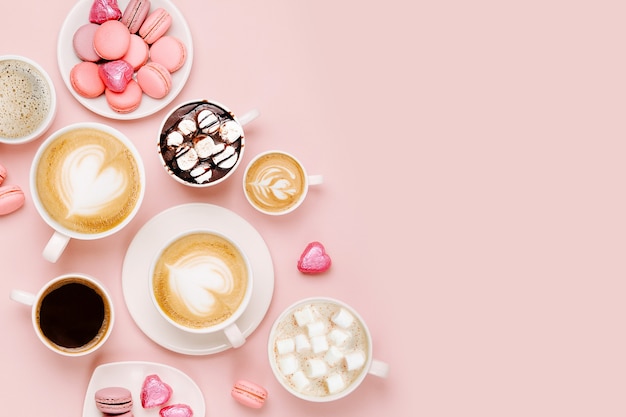 various kinds of coffee in cups of different size with candys and macaroons on pale pink background