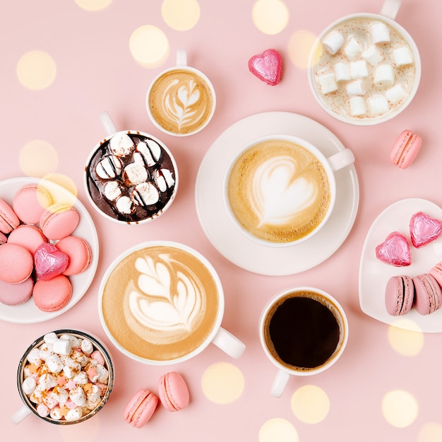 various kinds of coffee in cups of different size with candys and macaroons on pale pink background