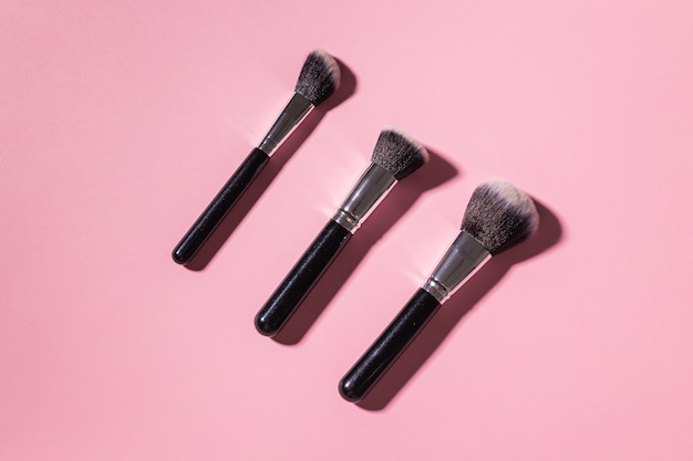 Various make-up brushes on pink background, top view. Cosmetics and beauty concept.