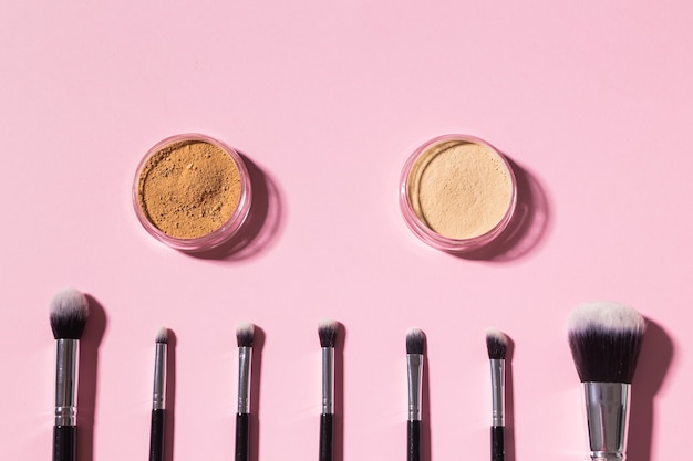 Various makeup brushes and face mineral powder on pink background with copy space top view cosmetics