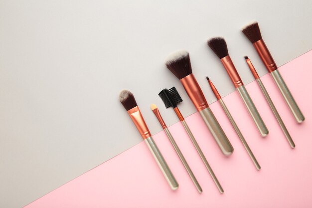 Various makeup brushes on grey and pink background with copy space. Top view