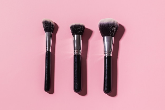 Various makeup brushes on pink background top view cosmetics and beauty concept