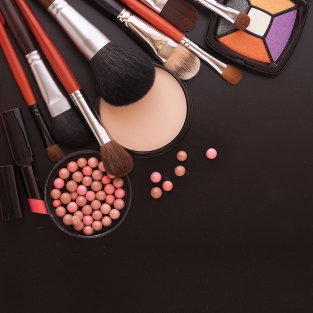 Various makeup products on dark black background with copyspace