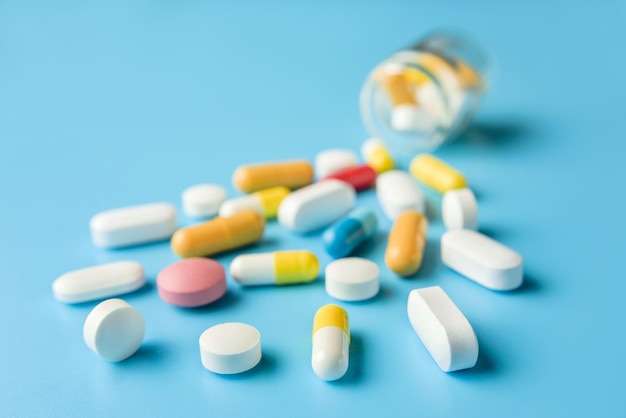 Various medicines scattered from a vial on a blue background. Macro composition with pills and capsules with selective focus.