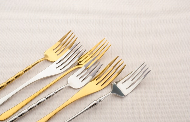 Various metal forks on a light table. Gold and silver cutlery, copy space