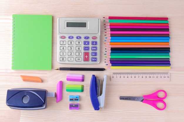 Various multi-colored stationery and school accessories on a natural wooden table. top view