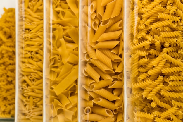 Various noodle sorts filled in high glasses against white background