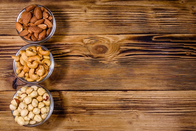 Varie noci (mandorle, anacardi, nocciole) in ciotole di vetro su un tavolo di legno. pasto vegetariano. concetto di alimentazione sana. vista dall'alto