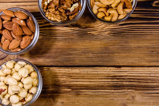 Various nuts (almond, cashew, hazelnut, walnut) in glass bowls on a wooden table. Vegetarian meal. Healthy eating concept. Top view