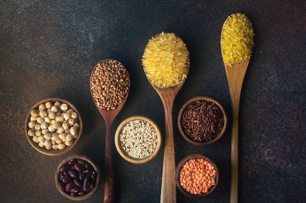 Various organic cereals and grains in wooden spoons and bowls on dark stone background. Rice, brown rice, buckwheat, millet, barley. Healthy diet, superfood, detox or vegetarian concept