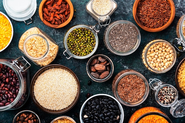 Various organic superfoods beans grains cereals legumes seeds in reusable cans and jars Copy space top view Blue background