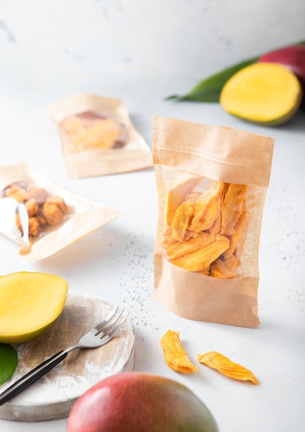 Various packages with sweet dried mango pieces and balls on light background